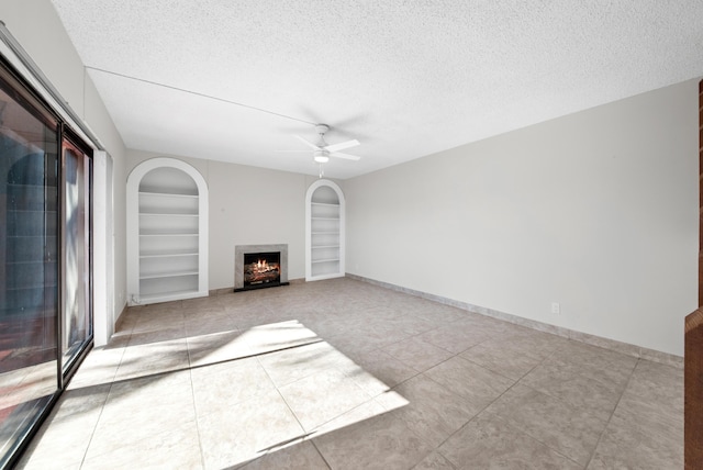 unfurnished living room featuring ceiling fan, light tile patterned flooring, built in features, and a textured ceiling