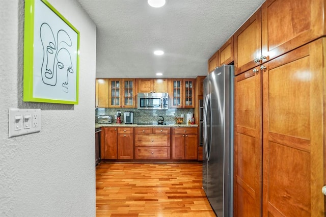 kitchen featuring decorative backsplash, appliances with stainless steel finishes, and light hardwood / wood-style flooring