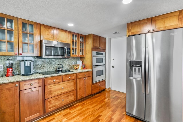 kitchen with backsplash, stainless steel appliances, light hardwood / wood-style flooring, and light stone counters