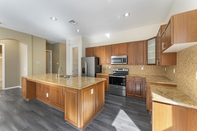 kitchen with dark wood-type flooring, sink, light stone countertops, an island with sink, and appliances with stainless steel finishes