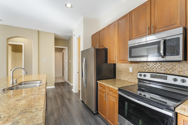 kitchen with appliances with stainless steel finishes, dark hardwood / wood-style flooring, tasteful backsplash, light stone counters, and sink