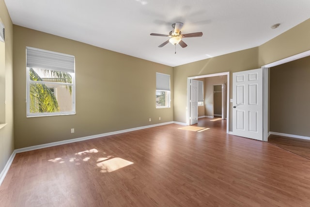 unfurnished bedroom featuring wood-type flooring, a spacious closet, multiple windows, and ceiling fan