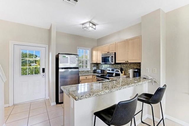 kitchen featuring stainless steel appliances, a kitchen breakfast bar, backsplash, kitchen peninsula, and light stone counters