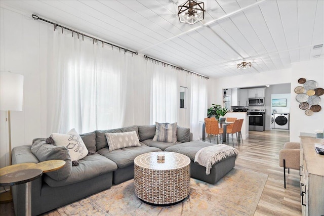 living room featuring washing machine and clothes dryer, wooden ceiling, and light wood-type flooring