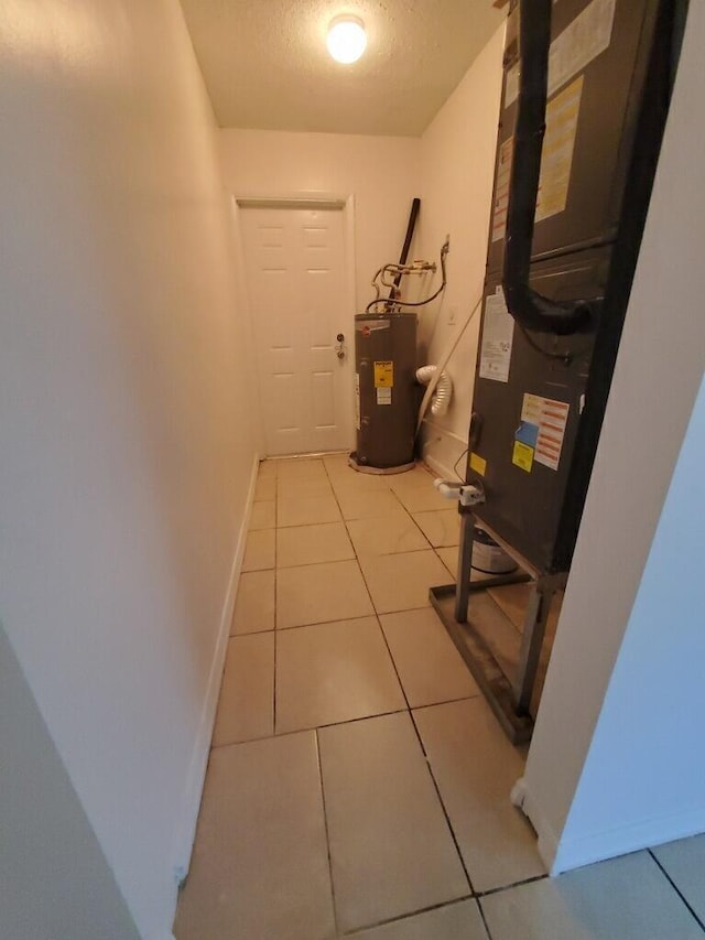 hallway with water heater, light tile patterned flooring, and a textured ceiling