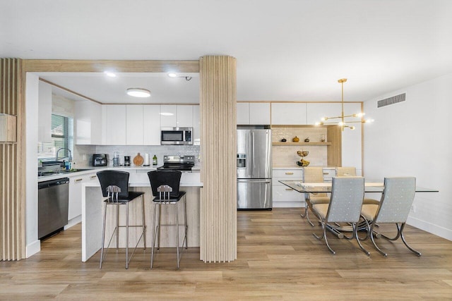 kitchen with white cabinetry, hanging light fixtures, stainless steel appliances, and light wood-type flooring