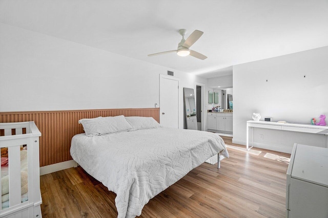 bedroom featuring connected bathroom, ceiling fan, wooden walls, and light hardwood / wood-style floors