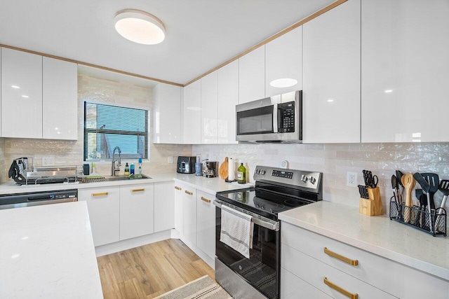 kitchen featuring appliances with stainless steel finishes, backsplash, sink, light hardwood / wood-style flooring, and white cabinets