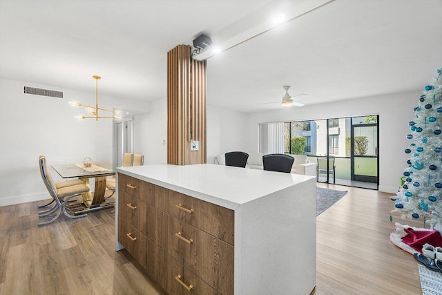 kitchen featuring ceiling fan with notable chandelier, a center island, light wood-type flooring, and hanging light fixtures