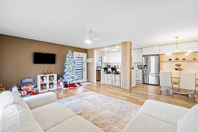 living room featuring ceiling fan with notable chandelier and light wood-type flooring