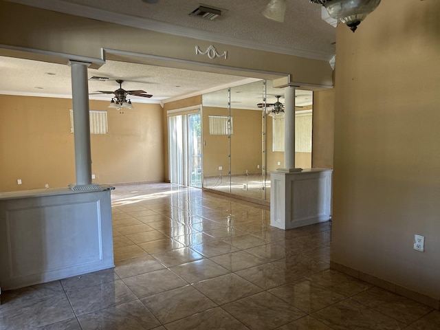 tiled empty room with crown molding, decorative columns, ceiling fan, and a textured ceiling