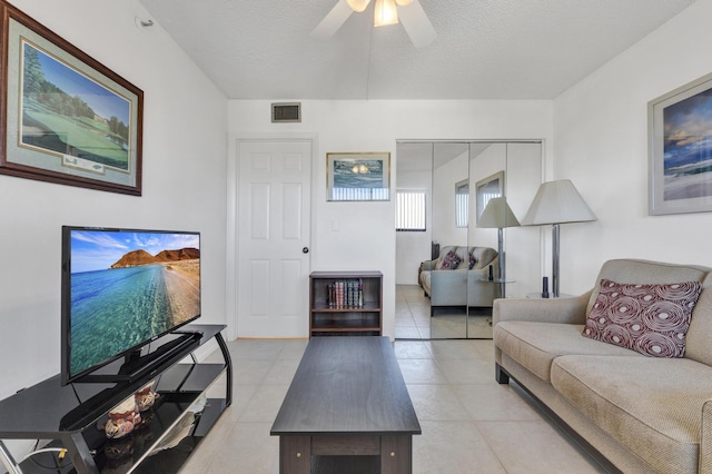 living room with ceiling fan, light tile patterned floors, and a textured ceiling