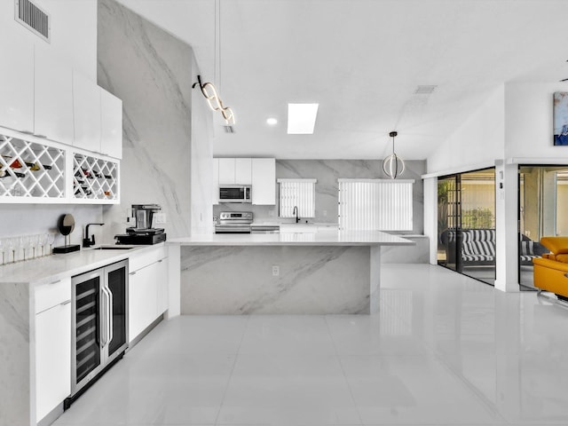 kitchen featuring hanging light fixtures, wine cooler, kitchen peninsula, white cabinets, and appliances with stainless steel finishes