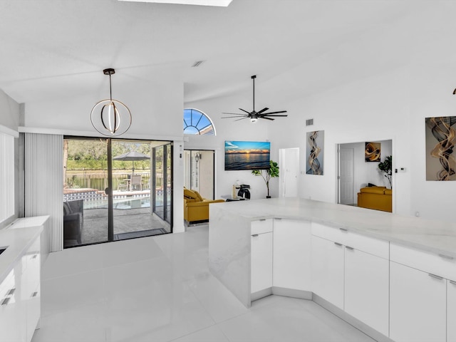 kitchen with ceiling fan with notable chandelier, light tile patterned floors, decorative light fixtures, light stone counters, and white cabinetry