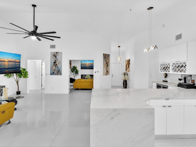 kitchen featuring light stone countertops, pendant lighting, a high ceiling, white cabinetry, and light tile patterned flooring