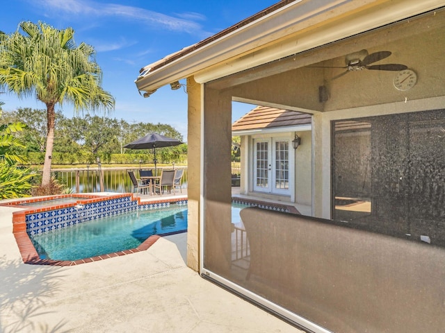 view of swimming pool with ceiling fan, a patio area, a water view, and an in ground hot tub