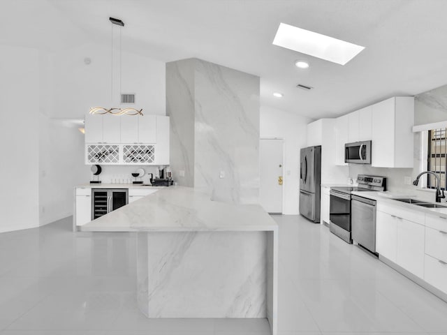 kitchen featuring sink, kitchen peninsula, lofted ceiling with skylight, white cabinets, and appliances with stainless steel finishes