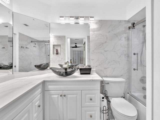 full bathroom featuring vanity, shower / bath combination with glass door, ceiling fan, toilet, and tile walls