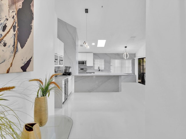 kitchen featuring a skylight, stainless steel appliances, hanging light fixtures, light tile patterned floors, and white cabinets