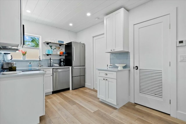 kitchen with white cabinets, decorative backsplash, appliances with stainless steel finishes, and light hardwood / wood-style flooring