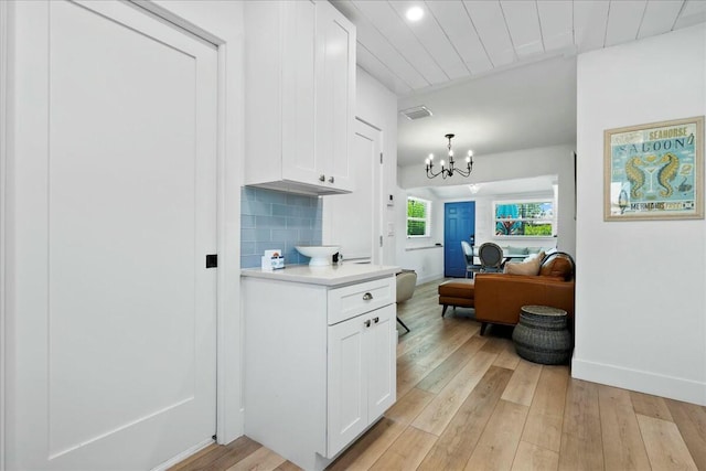 kitchen with backsplash, an inviting chandelier, white cabinets, decorative light fixtures, and light hardwood / wood-style floors