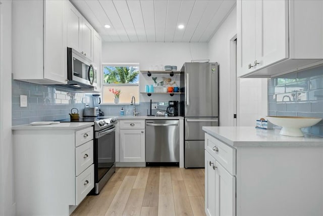 kitchen with sink, decorative backsplash, light wood-type flooring, appliances with stainless steel finishes, and white cabinetry