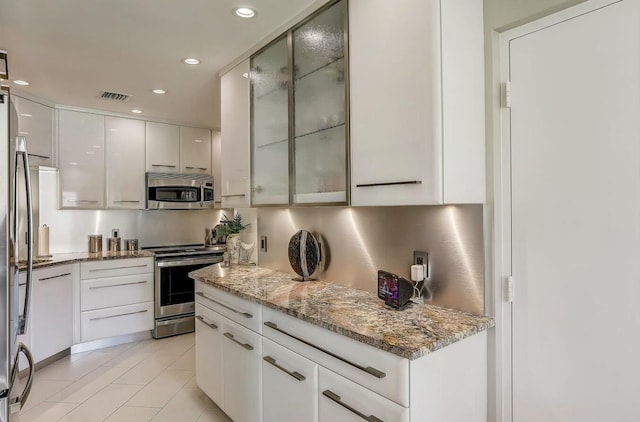 kitchen with appliances with stainless steel finishes, light tile patterned floors, white cabinetry, and light stone counters