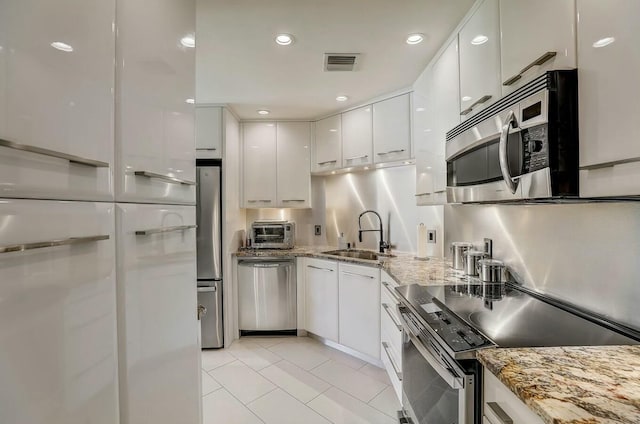 kitchen featuring light stone countertops, sink, stainless steel appliances, light tile patterned floors, and white cabinets