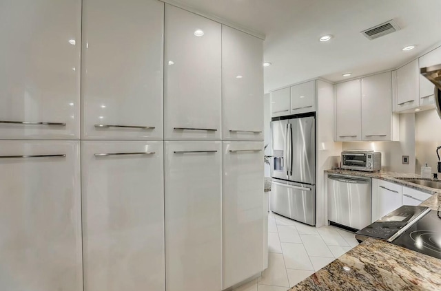 kitchen featuring sink, stainless steel appliances, light tile patterned floors, stone countertops, and white cabinets