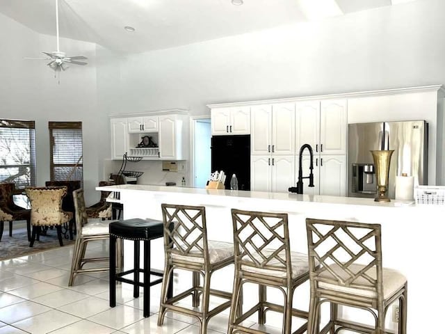 kitchen featuring stainless steel fridge, a kitchen breakfast bar, black fridge, high vaulted ceiling, and white cabinetry