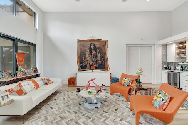 living room with hardwood / wood-style flooring, beverage cooler, a towering ceiling, and bar