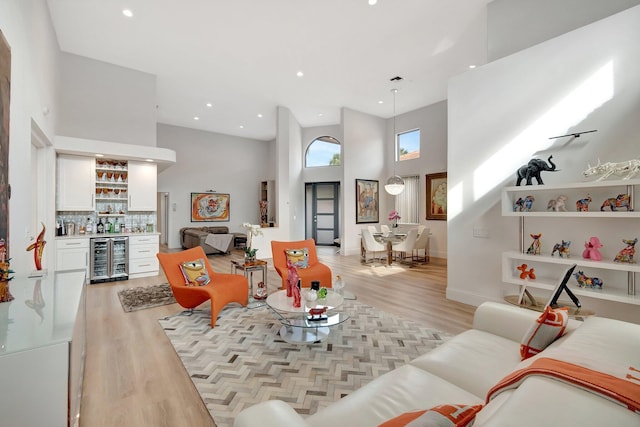 living room featuring bar area, light hardwood / wood-style flooring, beverage cooler, and a high ceiling