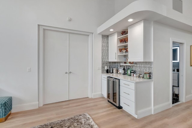 bar featuring backsplash, white cabinetry, beverage cooler, and light hardwood / wood-style floors