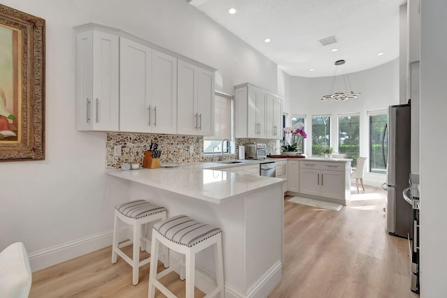 kitchen featuring kitchen peninsula, appliances with stainless steel finishes, sink, decorative light fixtures, and white cabinets