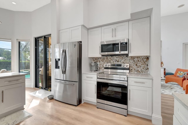 kitchen featuring white cabinets, light wood-type flooring, appliances with stainless steel finishes, and tasteful backsplash