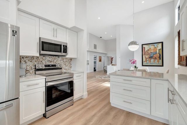 kitchen featuring pendant lighting, white cabinets, light wood-type flooring, a towering ceiling, and appliances with stainless steel finishes