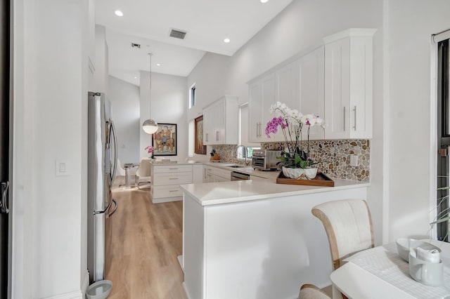 kitchen with backsplash, kitchen peninsula, pendant lighting, white cabinets, and light wood-type flooring