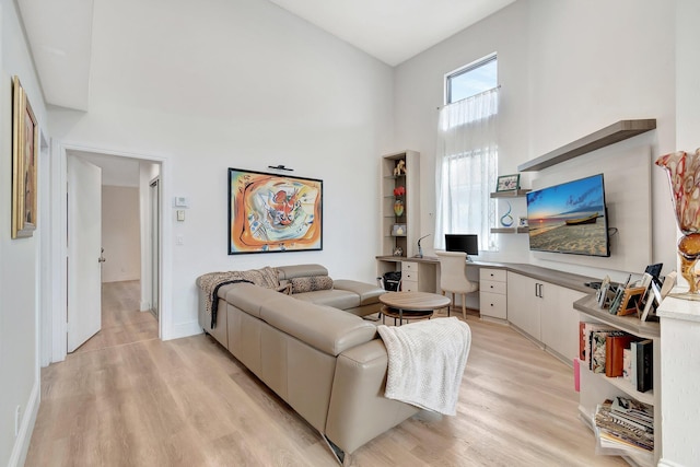 living room with a high ceiling, built in desk, and light hardwood / wood-style floors