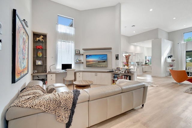 living room with light hardwood / wood-style floors, built in desk, and a high ceiling