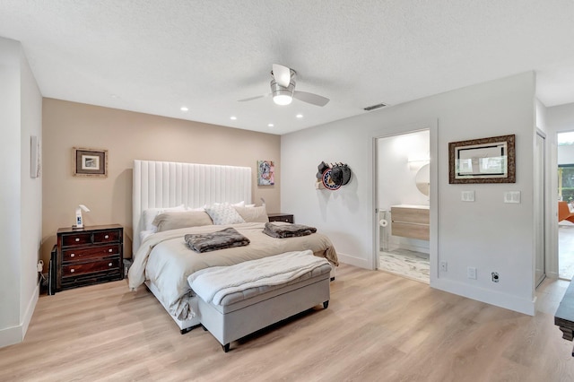 bedroom with a textured ceiling, light wood-type flooring, ensuite bath, and ceiling fan