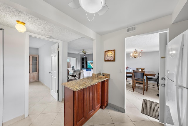 kitchen with light stone countertops, kitchen peninsula, white fridge, a textured ceiling, and light tile patterned floors