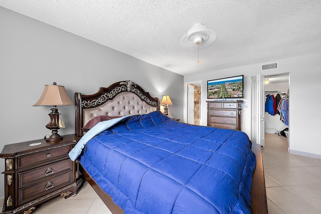 bedroom with a textured ceiling, ceiling fan, light tile patterned floors, a spacious closet, and a closet