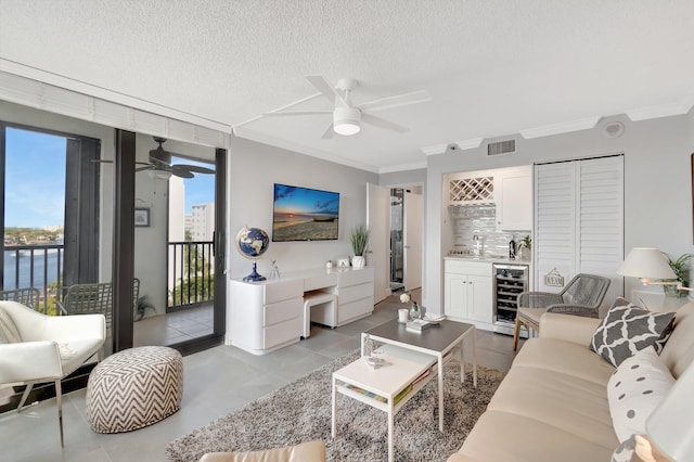 living room featuring wine cooler, indoor wet bar, crown molding, visible vents, and a textured ceiling