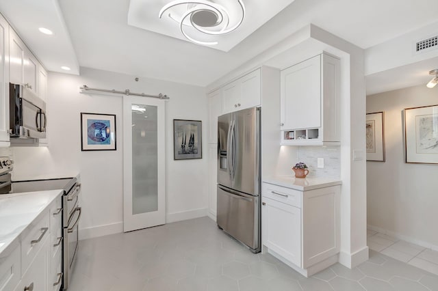 kitchen with tasteful backsplash, visible vents, a barn door, appliances with stainless steel finishes, and white cabinetry