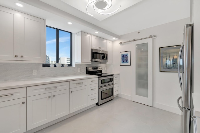 kitchen featuring a barn door, white cabinetry, light countertops, appliances with stainless steel finishes, and backsplash