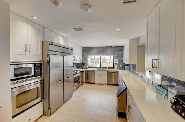 kitchen featuring light stone counters, visible vents, backsplash, white cabinets, and built in appliances