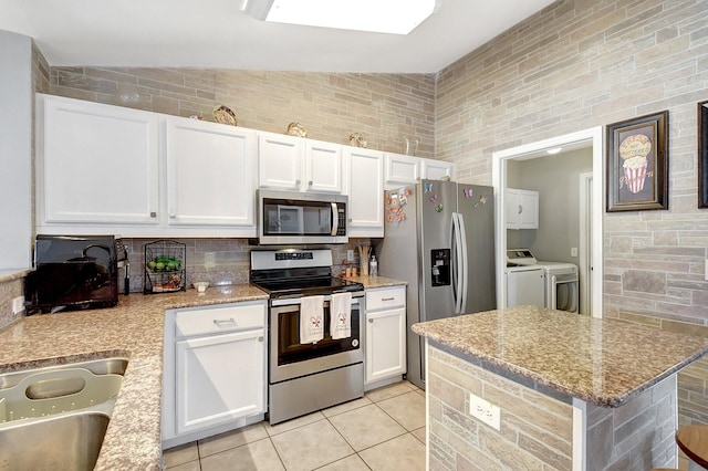 kitchen featuring light stone countertops, stainless steel appliances, vaulted ceiling, white cabinets, and washer and dryer