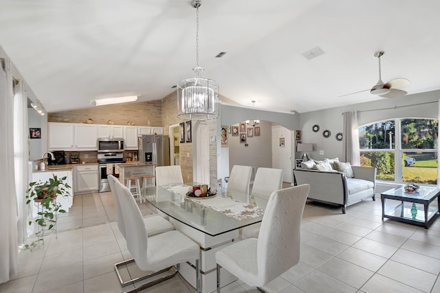 tiled dining area featuring ceiling fan with notable chandelier, lofted ceiling, and sink