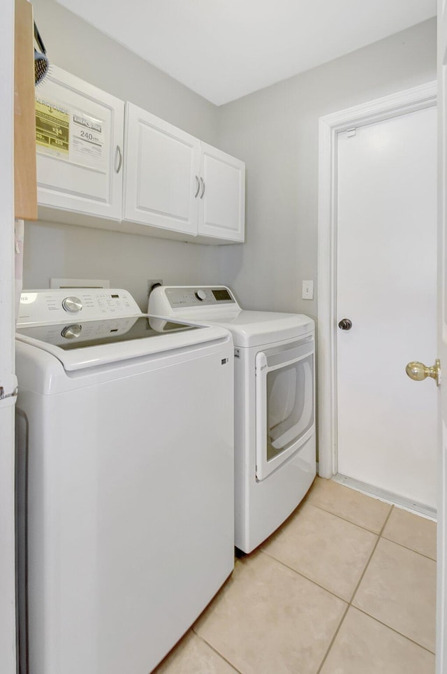 clothes washing area with light tile patterned flooring, cabinets, and washing machine and clothes dryer