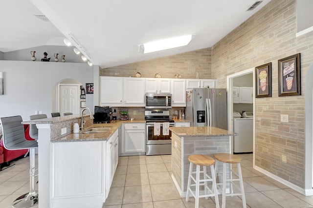 kitchen with a kitchen breakfast bar, white cabinets, stainless steel appliances, and brick wall